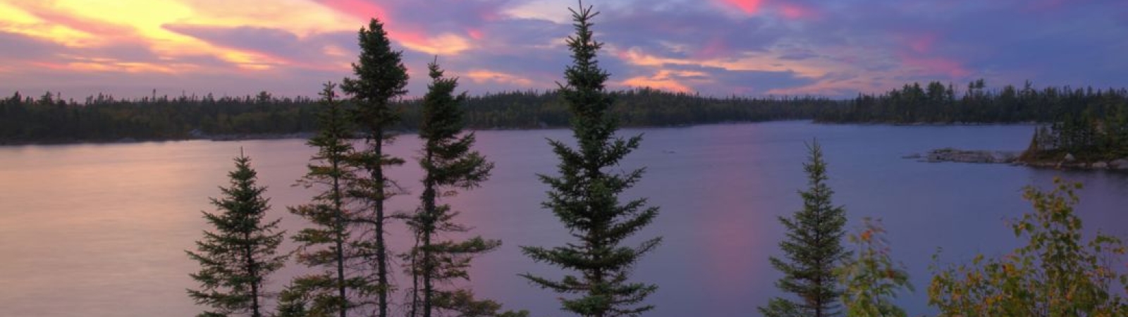 a lake surrounded by trees and rocks at sunset