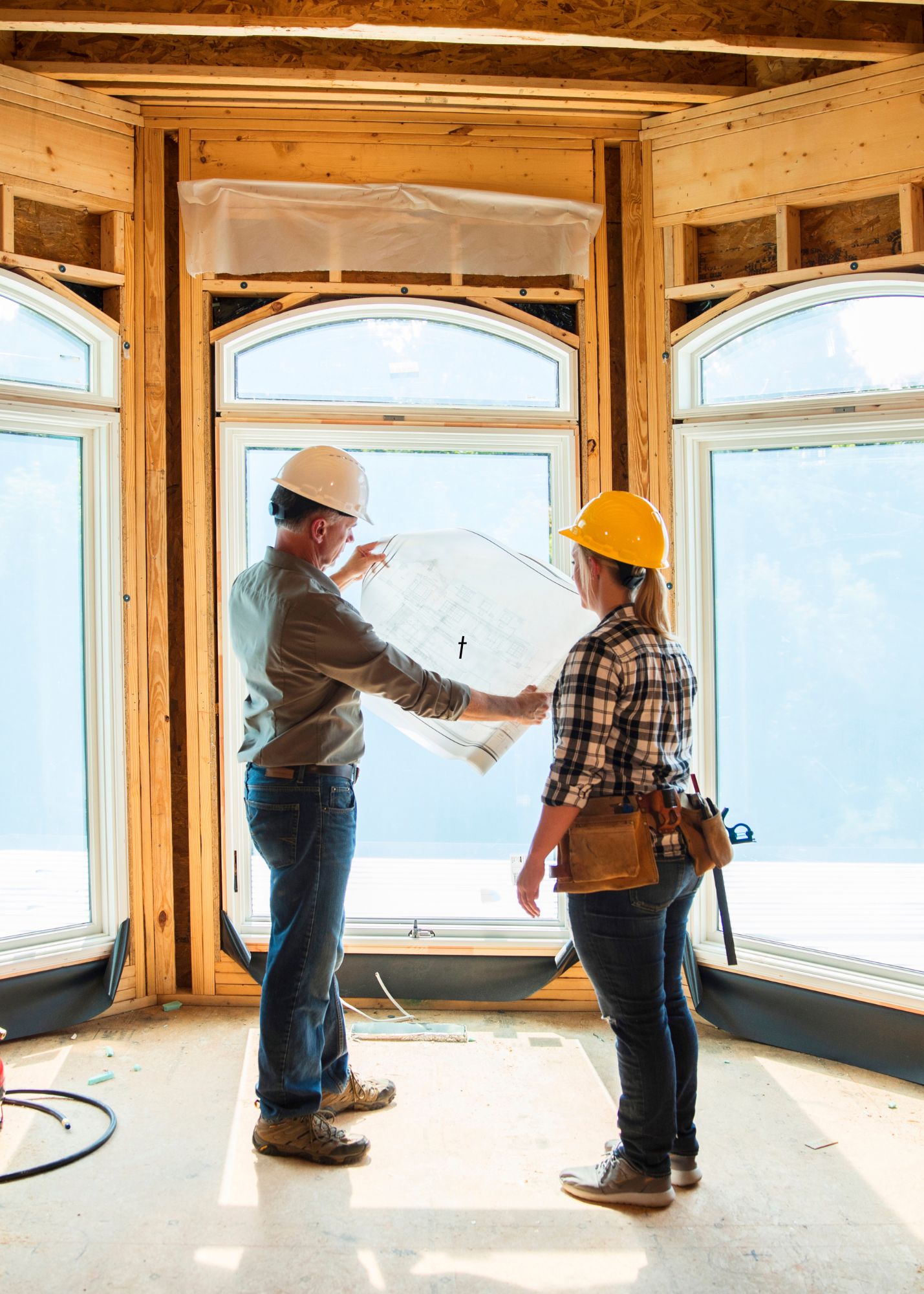 two construction workers stand looking at a sheet of paper in the window of a building under construction