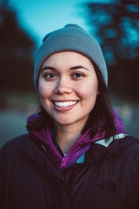 Danielle Moore, a young woman with black hair and brown eyes, smiles for the camera. She is wearing a purple hooded jacket and a greyish blue toque