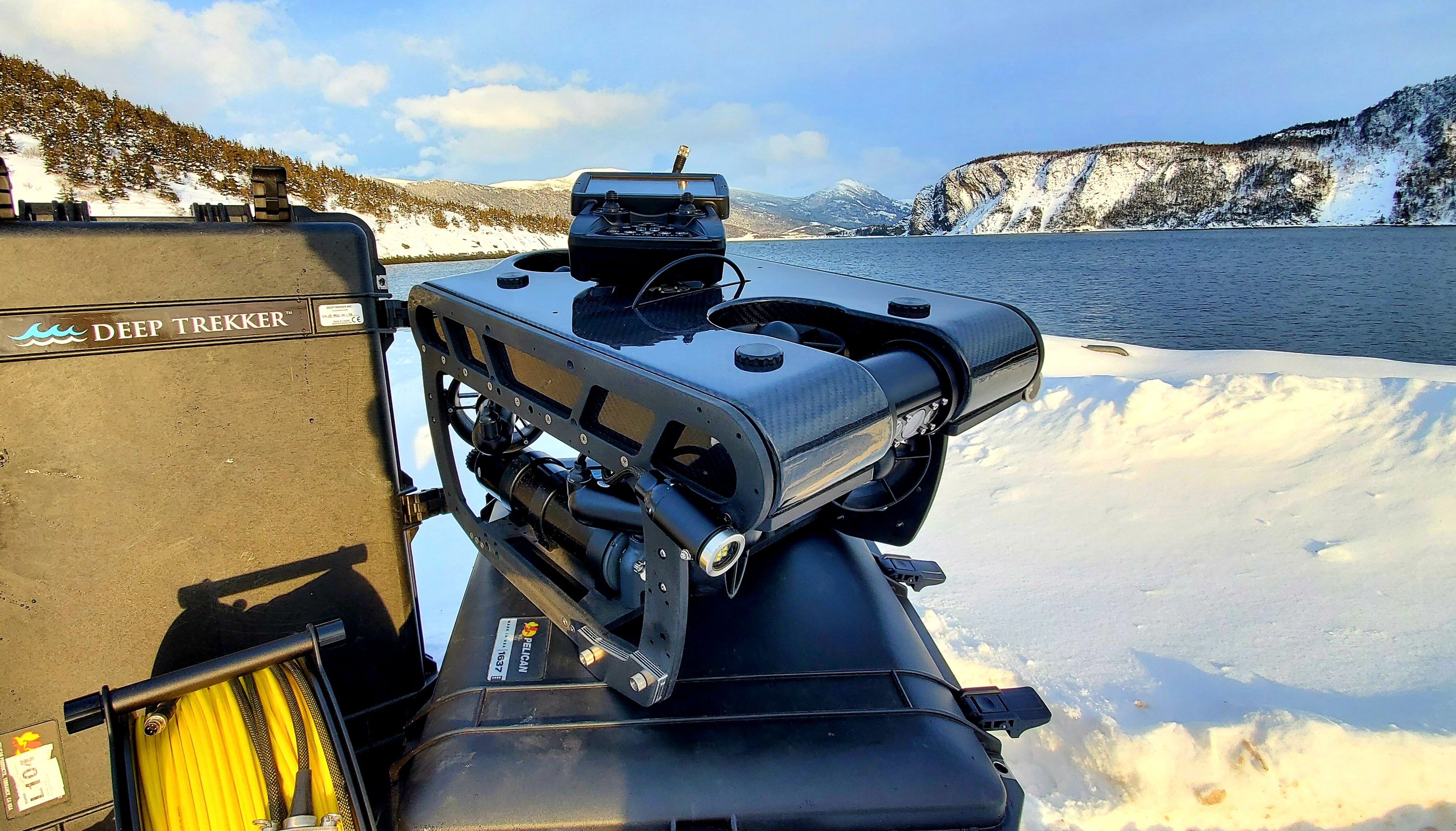 A ROV system is seen, with a snow-covered body of water, trees and cliffs in the background.