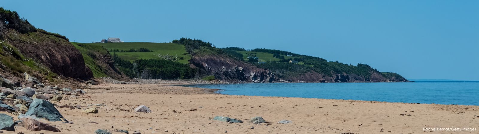 View of West Mabou Beach with rolling hillside, farm houses and blue sky in the background