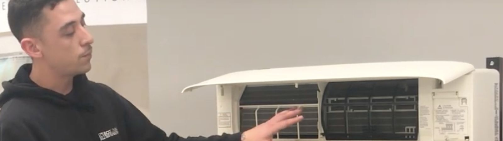 a man wearing a black hoodie gestures at a heat pump