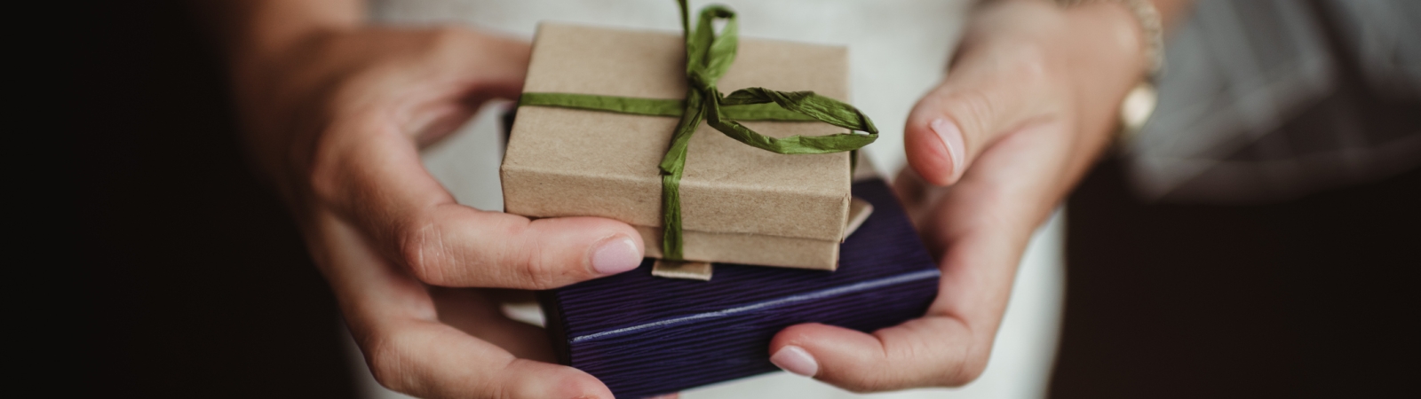 a person holding two small gift boxes. one is brown with a green ribbon and the other navy blue.