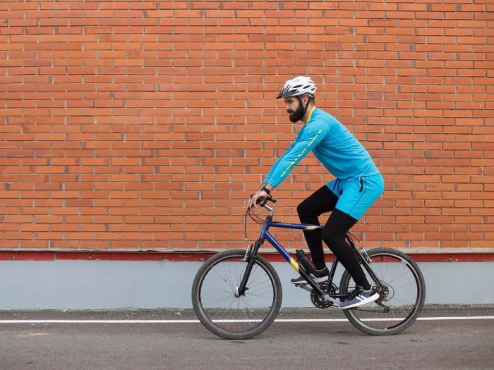 Person riding bicycle with a helmet and a brick wall behind them.