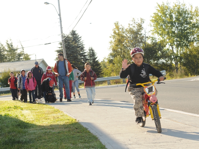 A group of children walking to school on a sidewalk on a nice day.