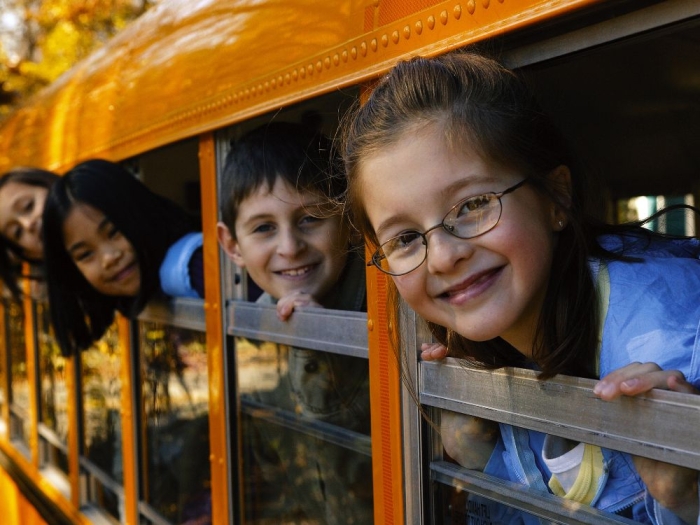 Four smiling children look out the windows of a school bus