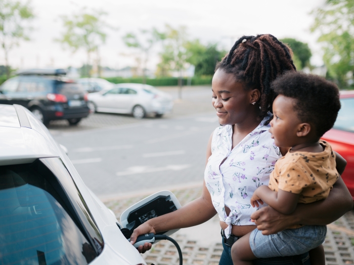Young adult mother charging her electric car parked next to the charging station and holding her baby son in her other hand