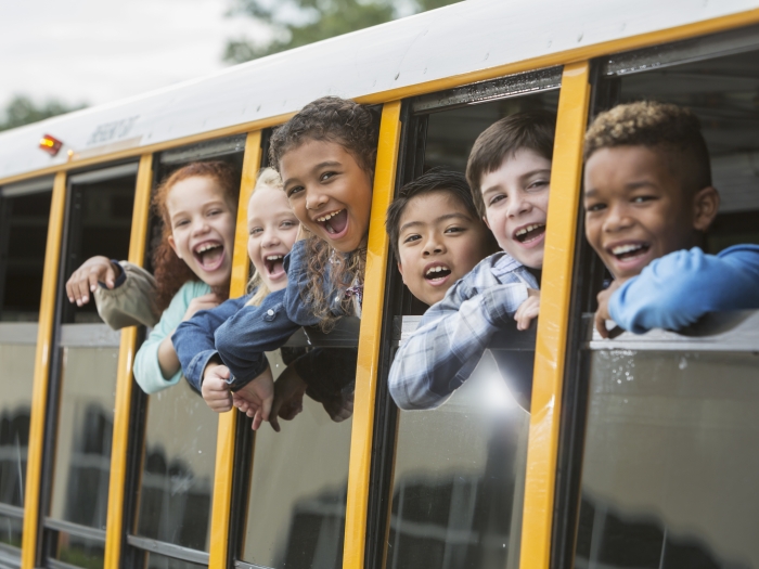 six laughing children in a school bus with the windows down.