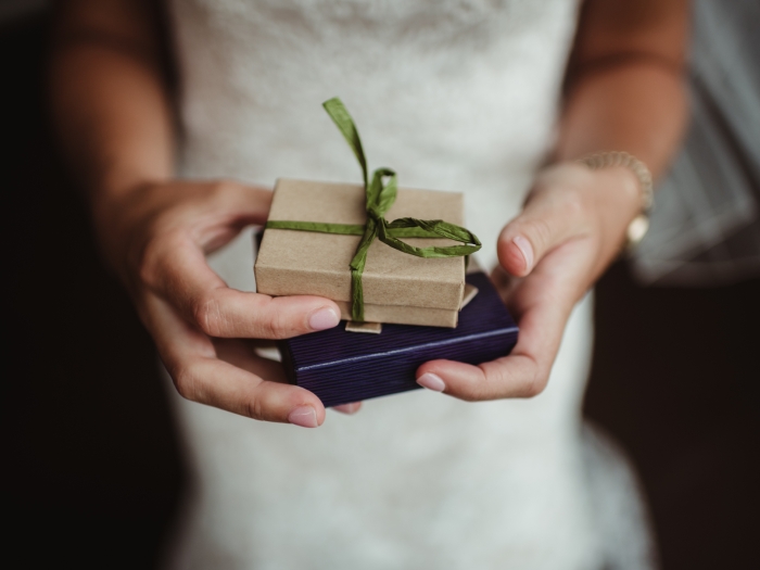 a person holding two small gift boxes. one is brown with a green ribbon and the other navy blue.