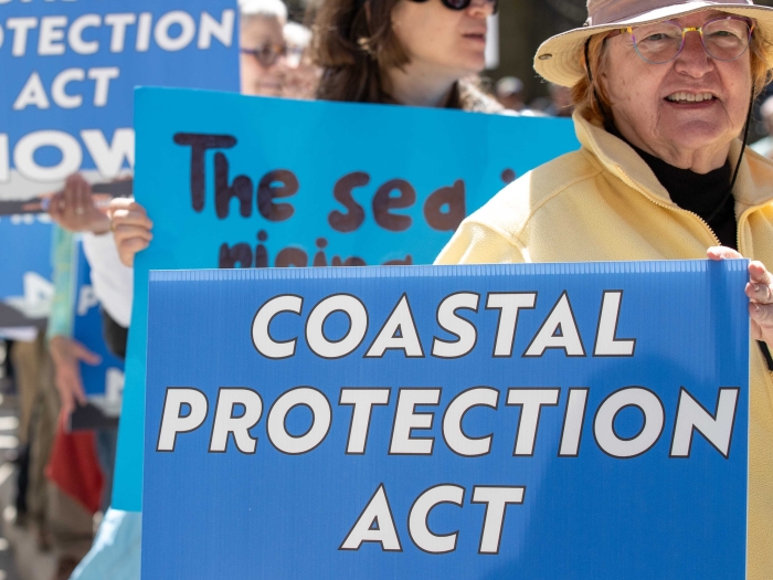 people standing outside holding signs that read "Coastal Protection Act NOW"