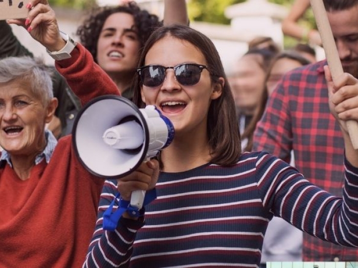 woman with a megaphone at a rally next to someone with a sign that says "We Need a Change"