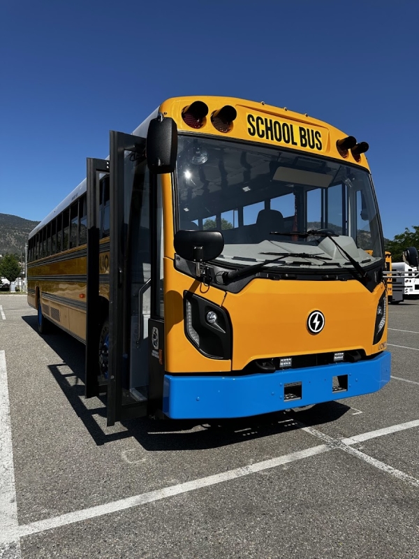 An electric school bus in a parking lot under a clear blue sky